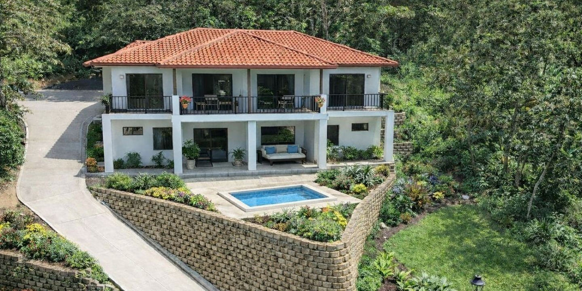 Aerial view of Yuma 26: two-storey home with terracotta roof and pool terrace above a stone retaining wall